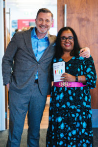 Thomas Erikson and Advita Patel are smiling brightly towards the camera. Advita is holding a copy of Thomas' book in her hands - Surrounded by Idiots which talks about DISC styles.